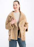 Woman wearing an oversized camel shearling jacket with wide lapels and large front patch pockets by Lebeni.