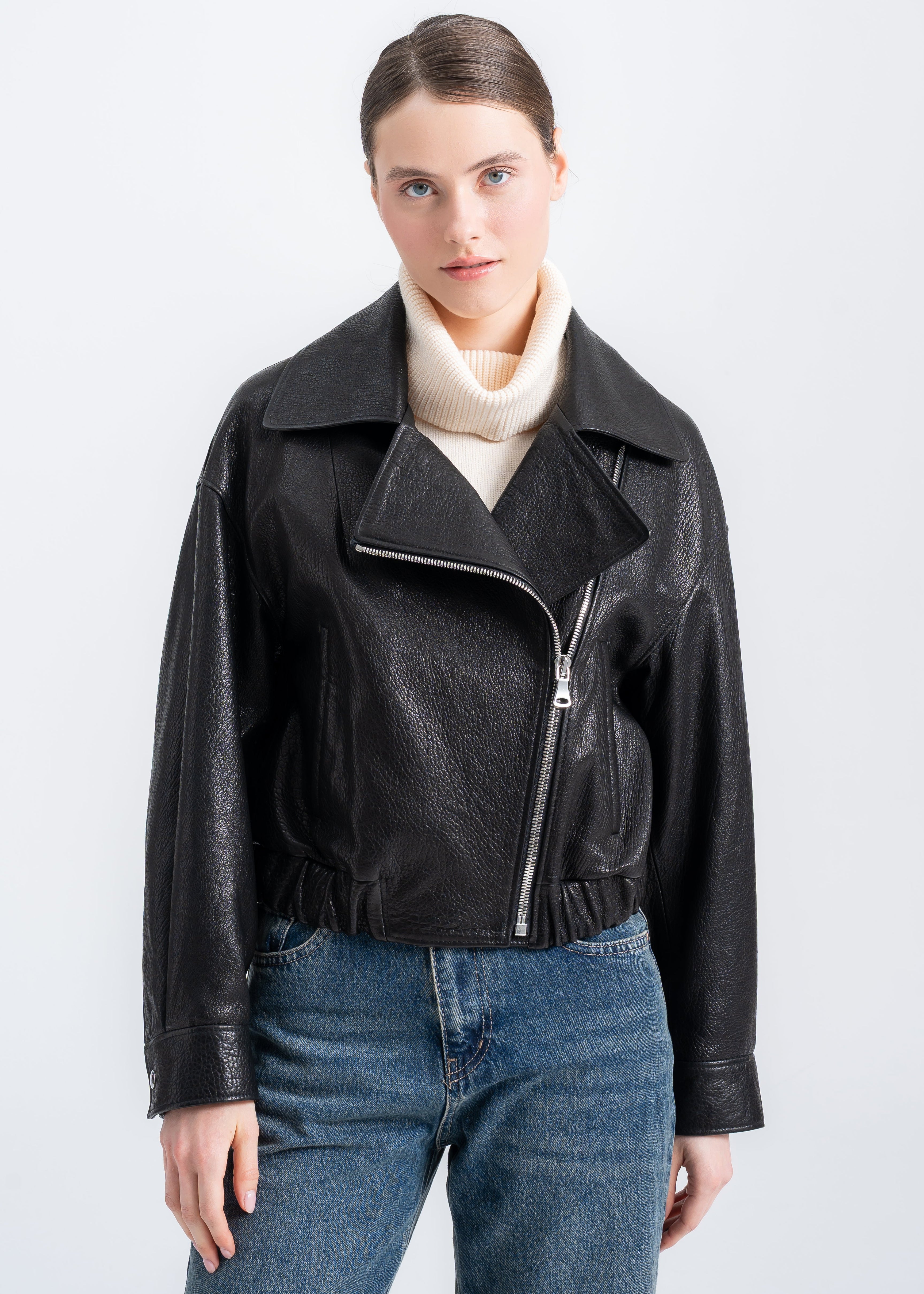 Model wearing a cropped black textured lambskin leather jacket with wide lapel collar and asymmetric zip closure. by Lebeni Leather Store