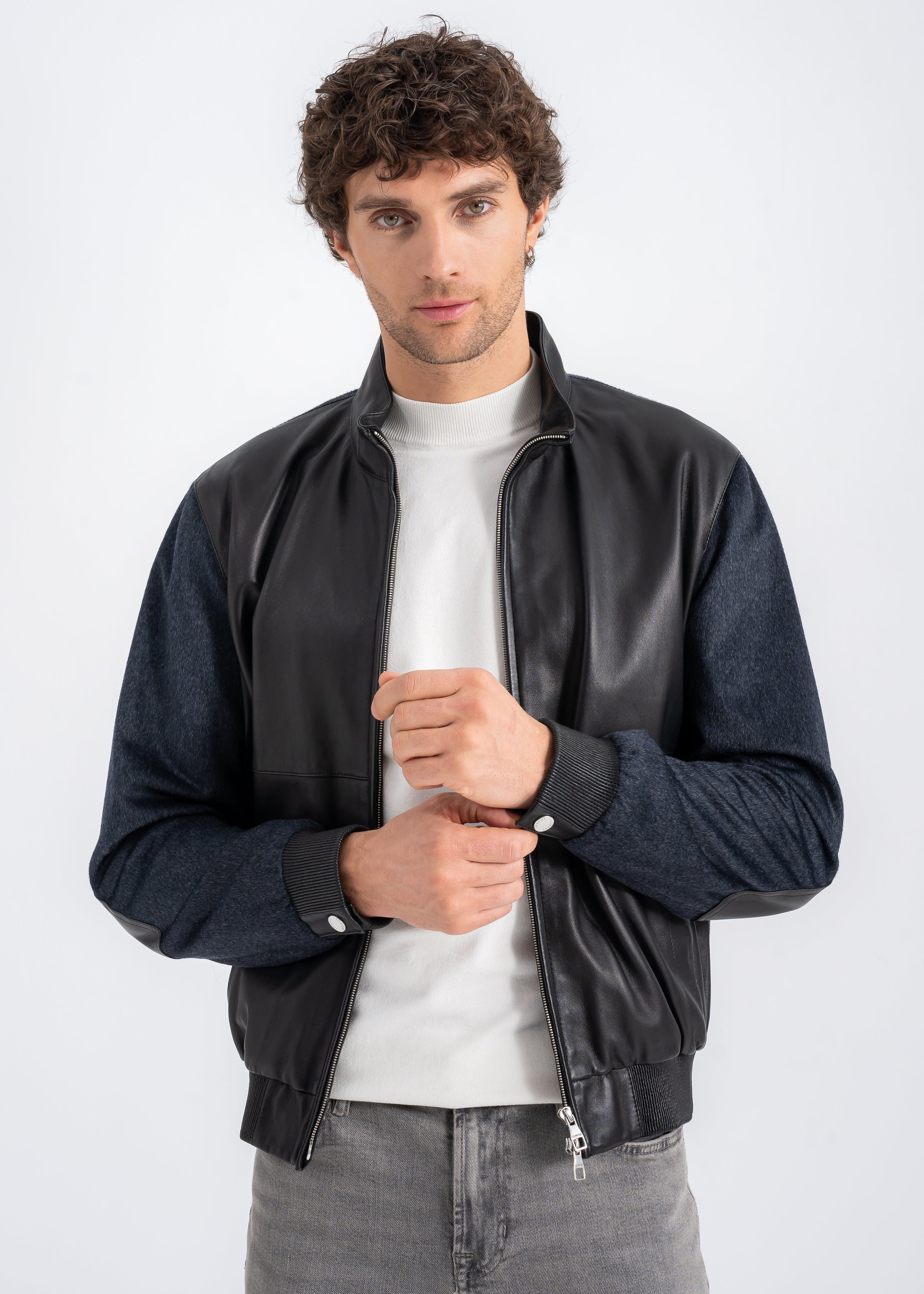 Model wearing a men’s black lambskin and dark navy wool bomber jacket with zip front, ribbed hem, and side zip pockets by Lebeni.

