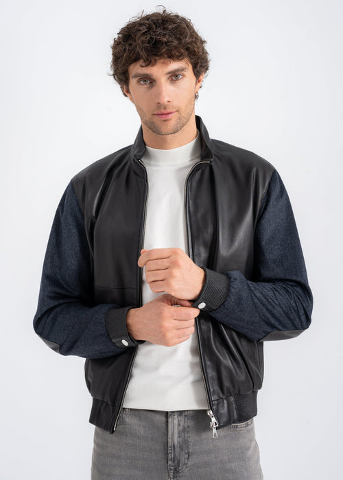 Model wearing a men’s black lambskin and dark navy wool bomber jacket with zip front, ribbed hem, and side zip pockets by Lebeni.

