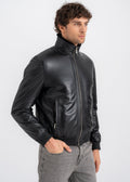 Male model wearing a black lambskin bomber jacket with shearling lined interior, front zipper, zip pockets, and rib knit hem by Lebeni.
