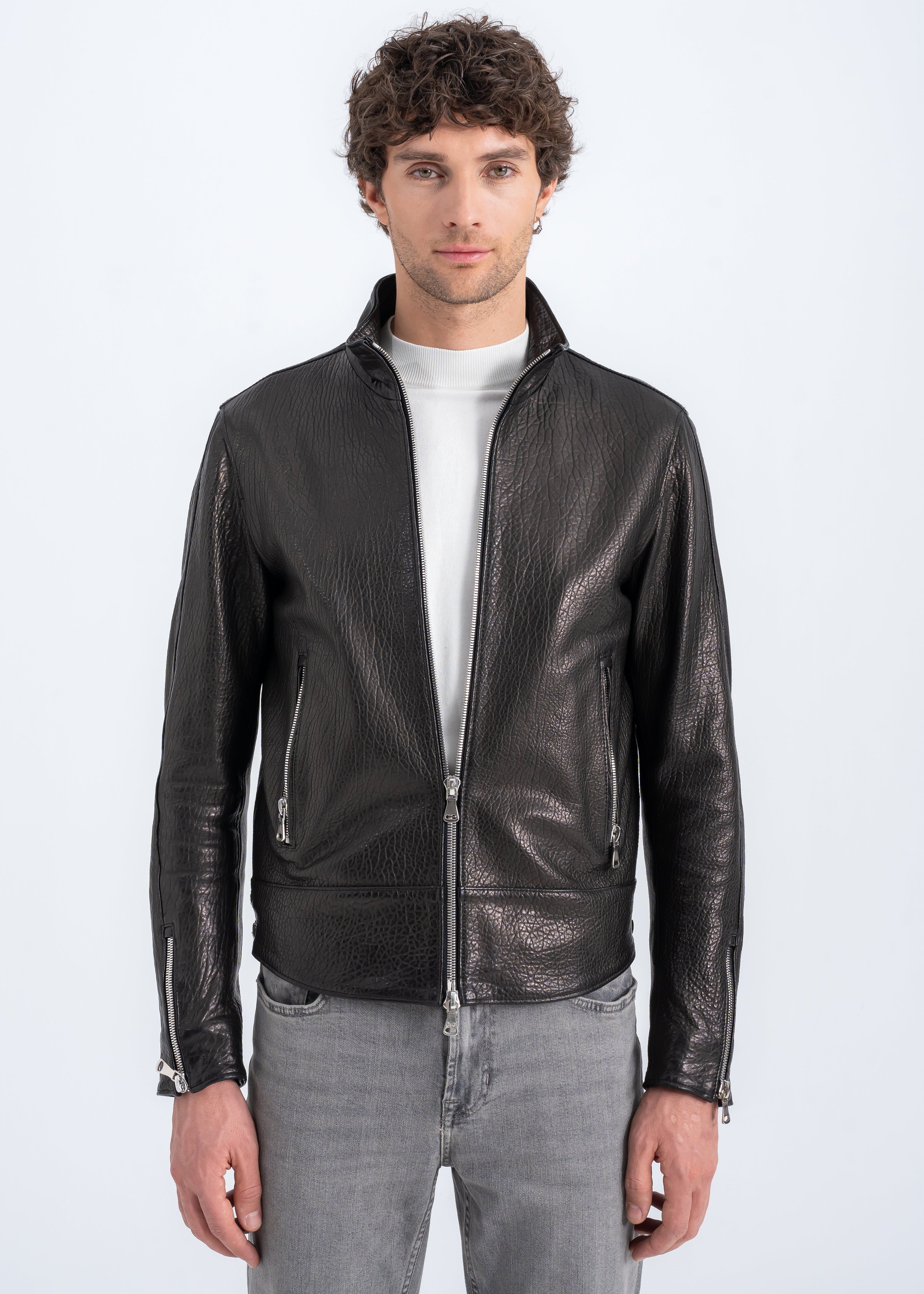 Model wearing a men’s black textured lambskin biker jacket with two way front zipper, zip pockets, zip cuffs, and side hem zips by Lebeni.