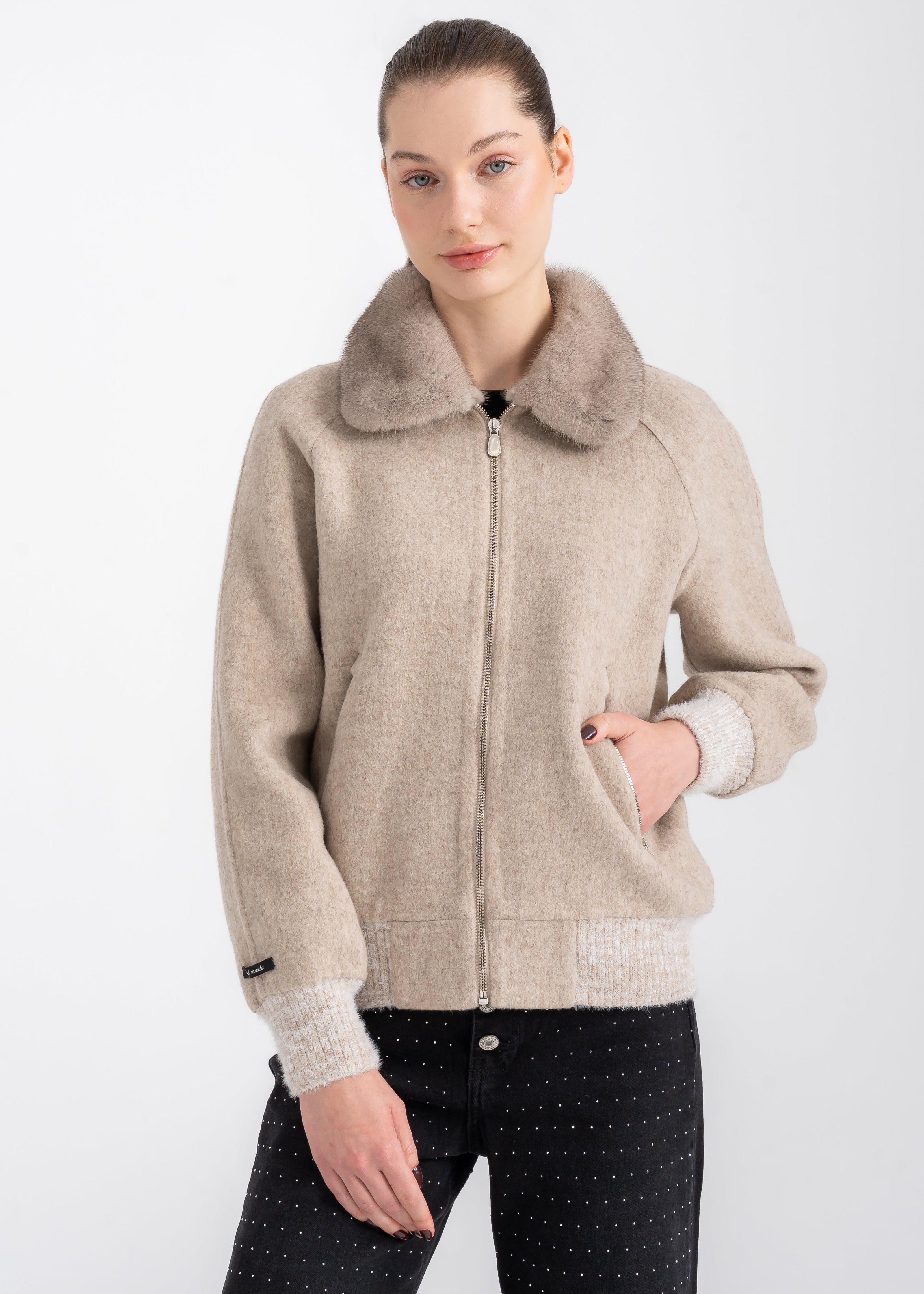 Woman wearing a beige alpaca bomber jacket with taupe mink fur collar, front zipper, knit rib cuffs and hem, styled with black trousers by Lebeni.