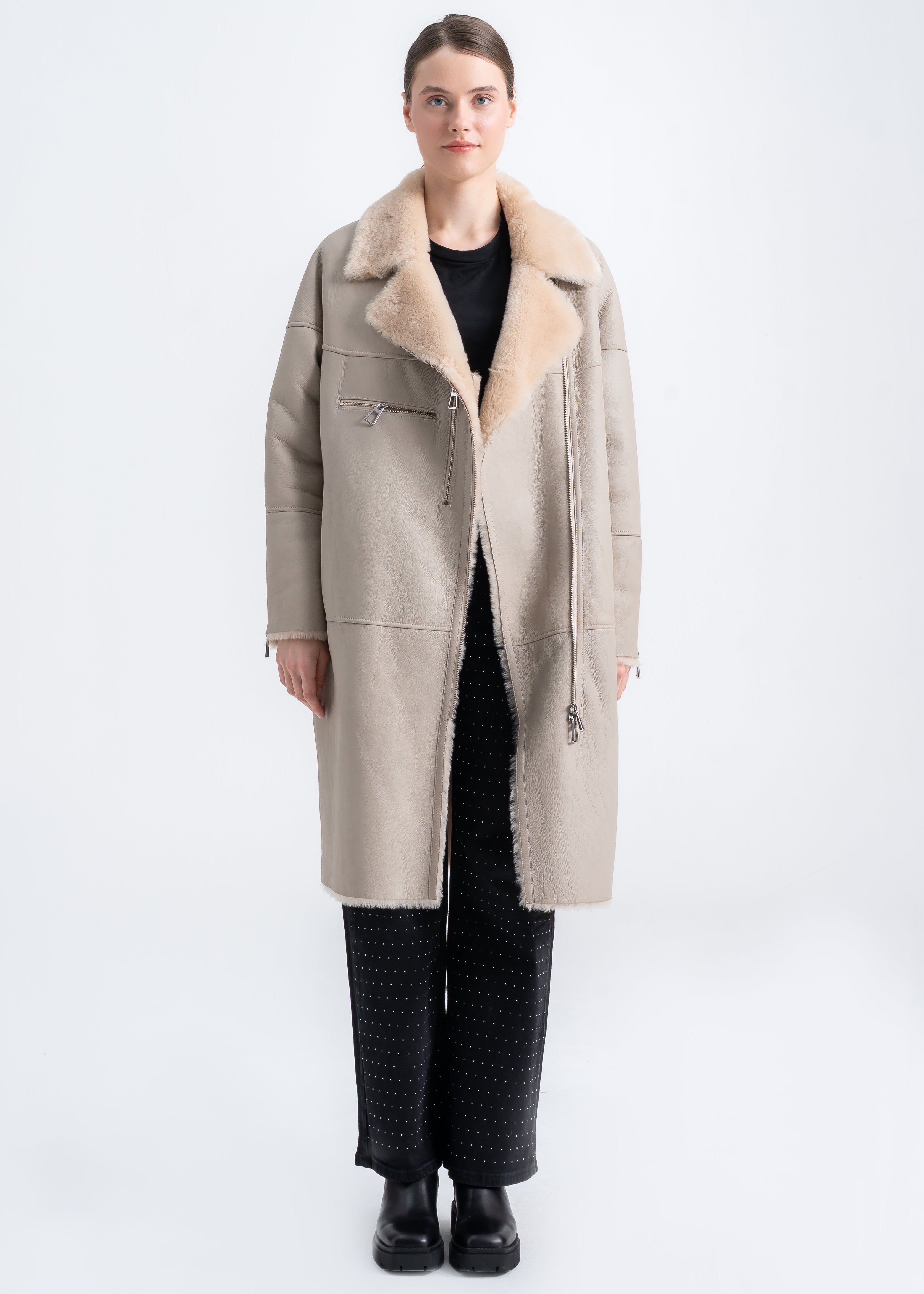 Woman wearing a beige long shearling leather coat with wide shearling collar and asymmetric front zipper by Lebeni.