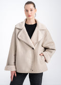 Woman wearing a relaxed light beige shearling jacket with wide lapels, turned up shearling cuffs and front welt pockets by Lebeni.