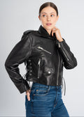 Woman wearing a black lamb leather cropped biker jacket with side lacing, silver zippers, flap pocket and shoulder epaulettes styled with blue denim jeans by Lebeni.