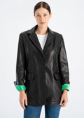 Woman wearing a long black lambskin leather blazer with hidden magnetic front button, tailored hip length fit and bright green satin lining visible at the cuffs by Lebeni.
