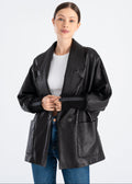 Woman wearing a black oversized lambskin leather jacket with wide lapel collar, single concealed magnetic button, large front patch pockets and rib knit cuffs by Lebeni.