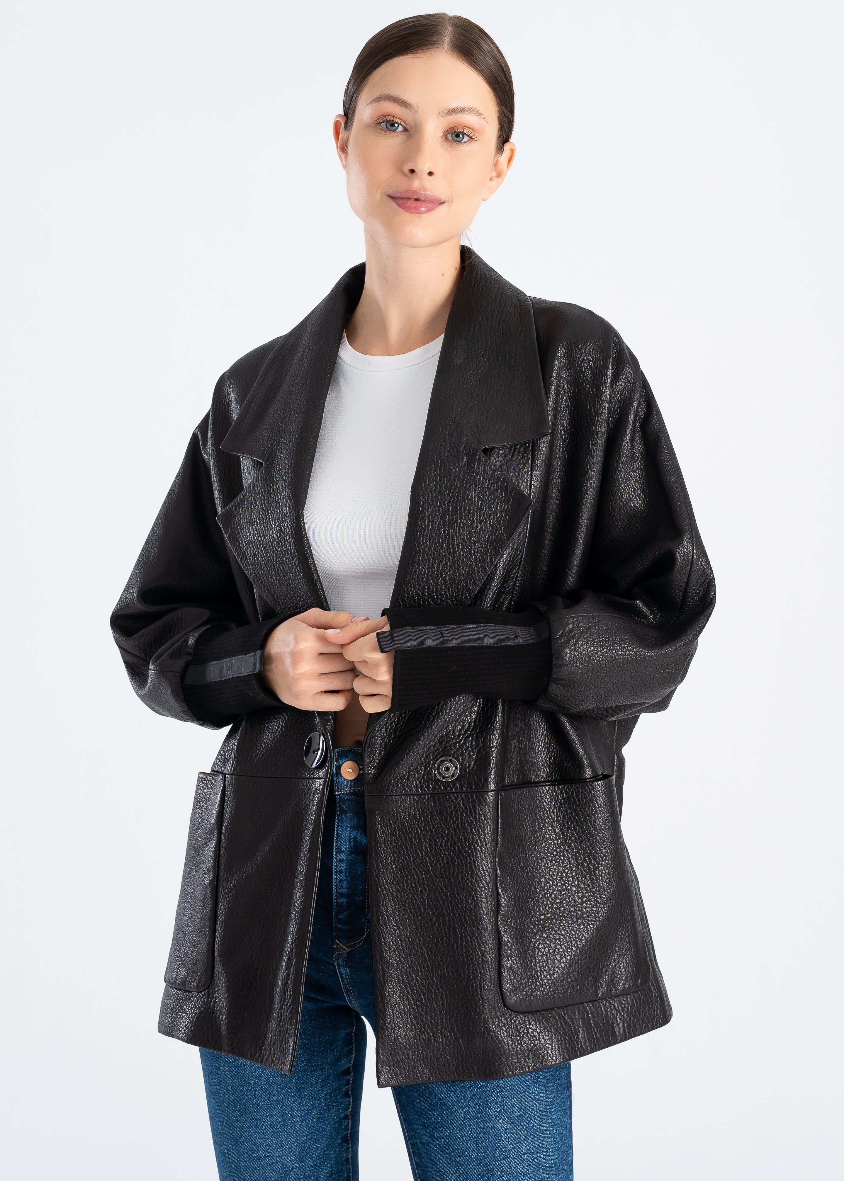 Woman wearing a black oversized lambskin leather jacket with wide lapel collar, single concealed magnetic button, large front patch pockets and rib knit cuffs by Lebeni.