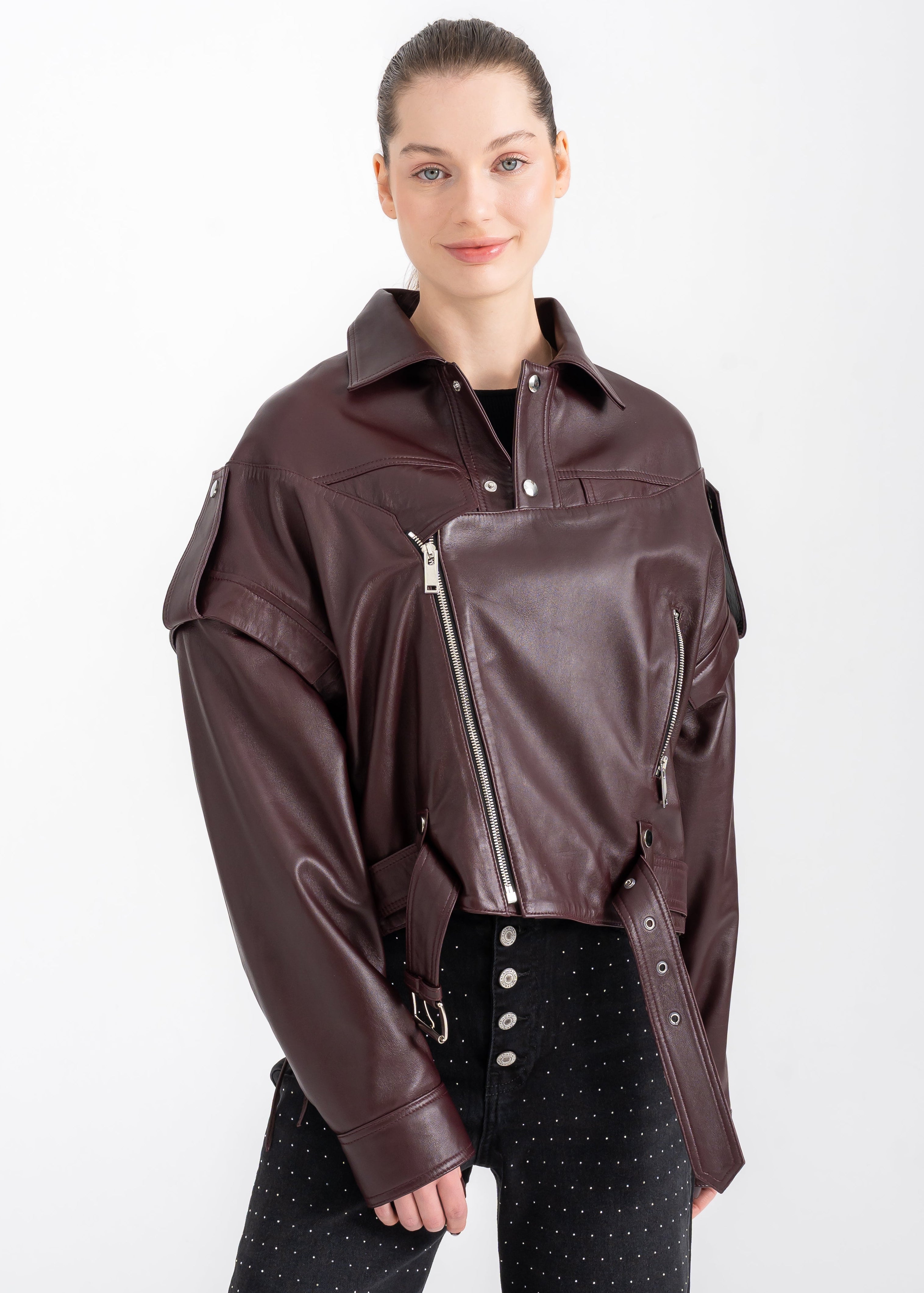 Model wearing a burgundy lambskin cropped biker jacket with asymmetric zipper and back lacing, silver hardware, by Lebeni.