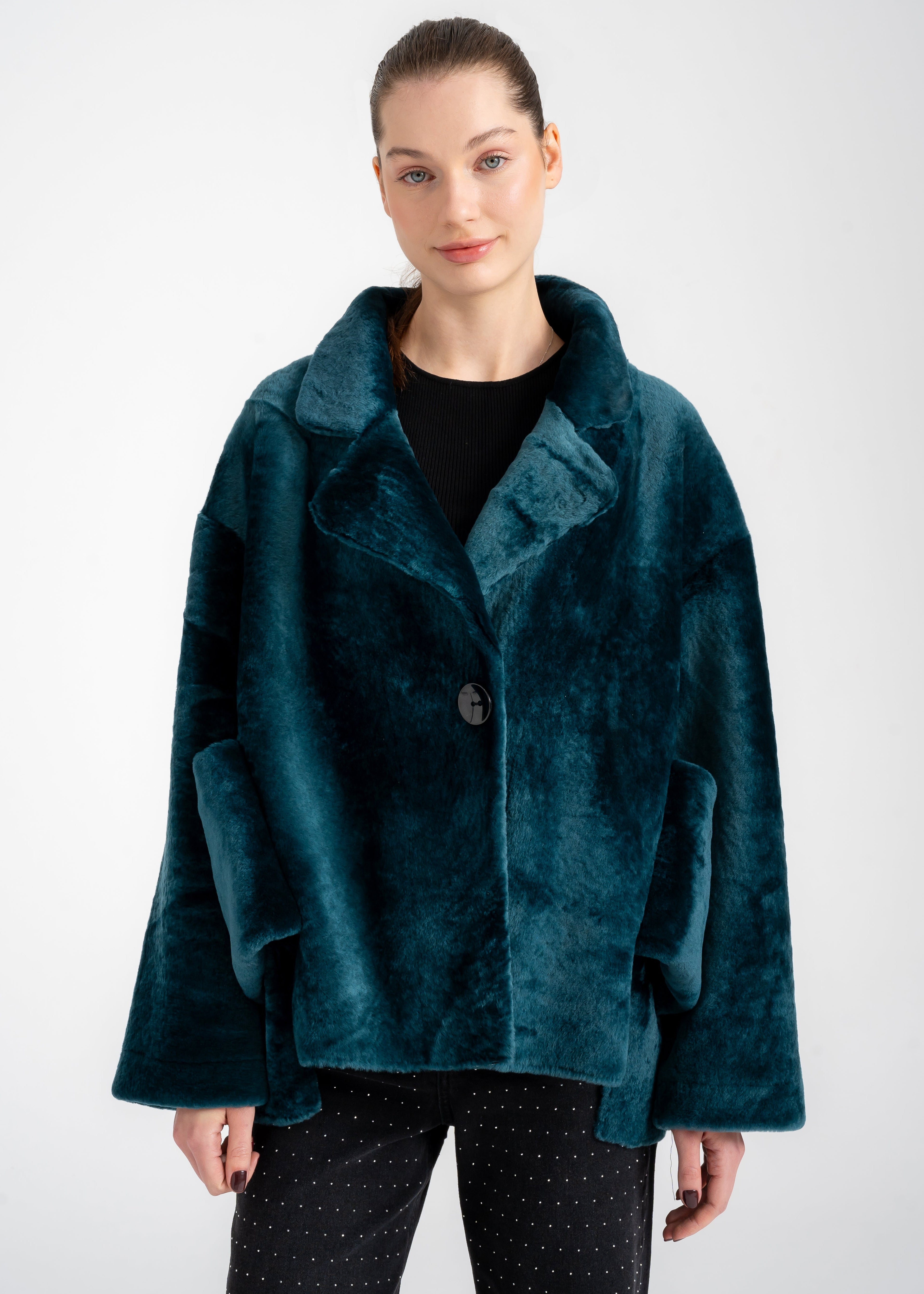 Model wearing a deep teal shearling coat with wide collar, single button closure, and oversized front patch pockets by Lebeni.