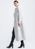 Woman wearing a light grey long shearling coat with notch collar, front button closure and relaxed full length silhouette by Lebeni.
