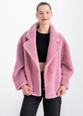 Woman wearing an oversized soft pink shearling jacket with wide lapels and large front patch pockets by Lebeni.