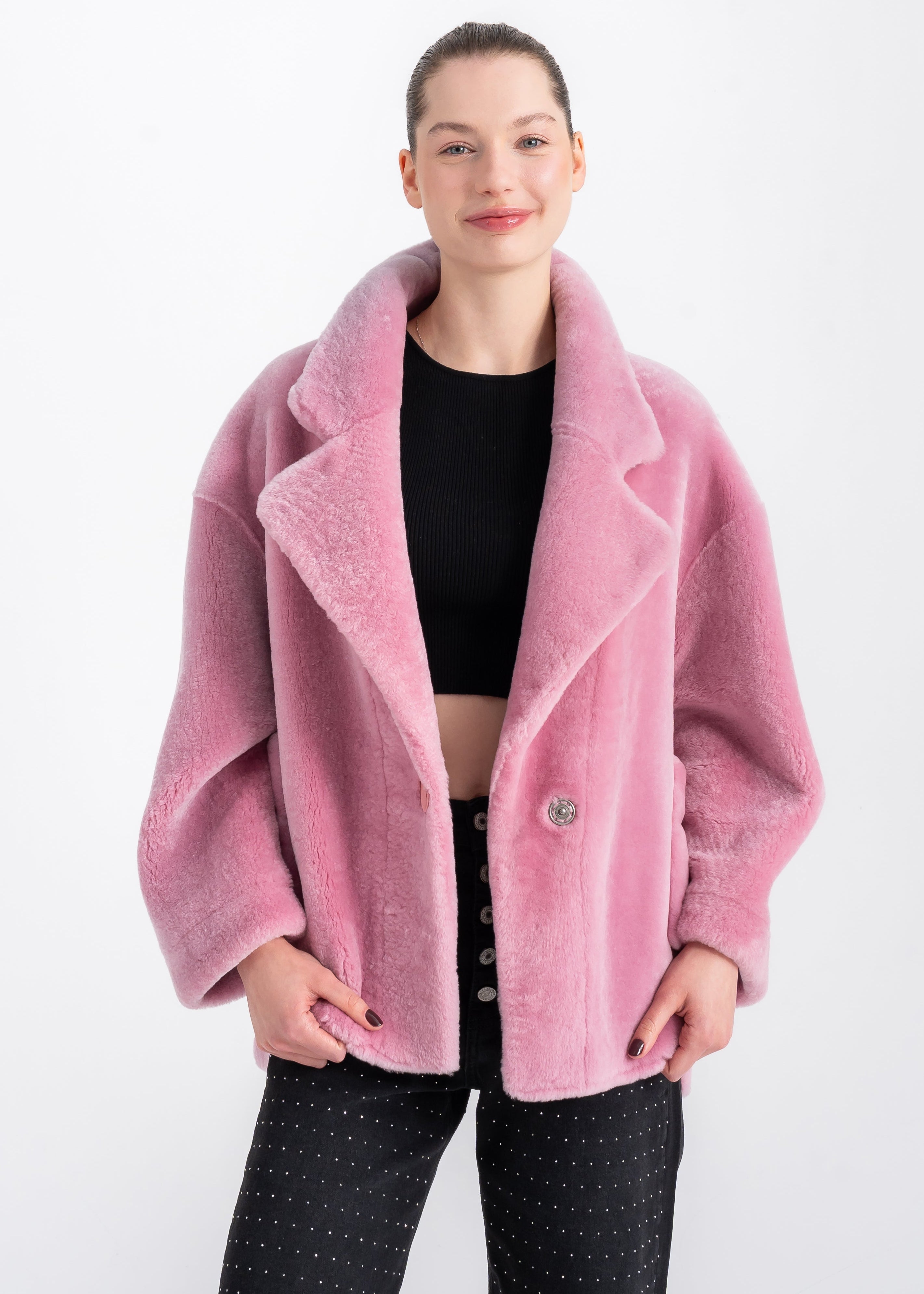 Woman wearing an oversized soft pink shearling jacket with wide lapels and large front patch pockets by Lebeni.