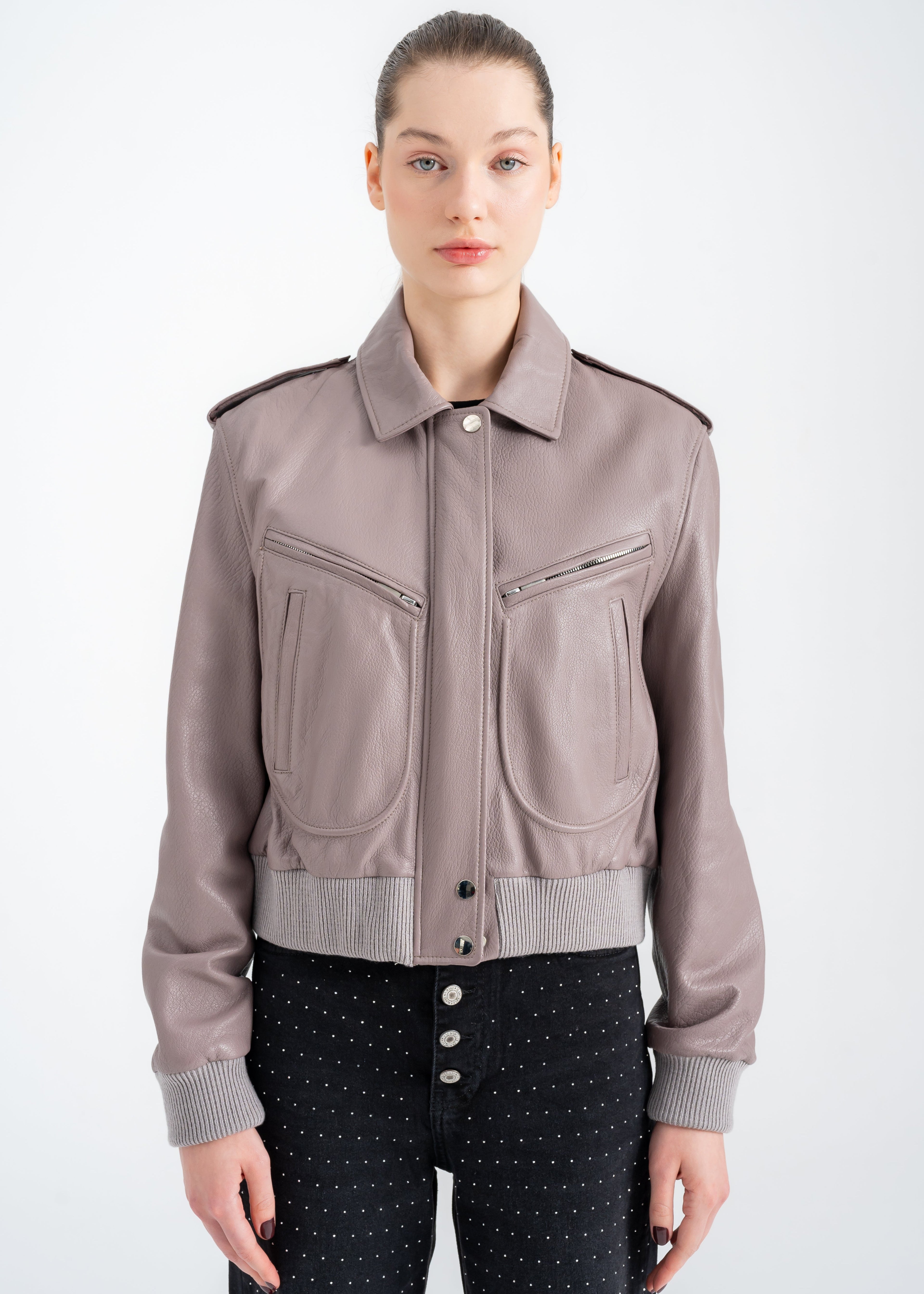 Model wearing a taupe lambskin utility bomber jacket with cropped ribbed hem, epaulettes, and mixed zip and welt pockets by Lebeni.