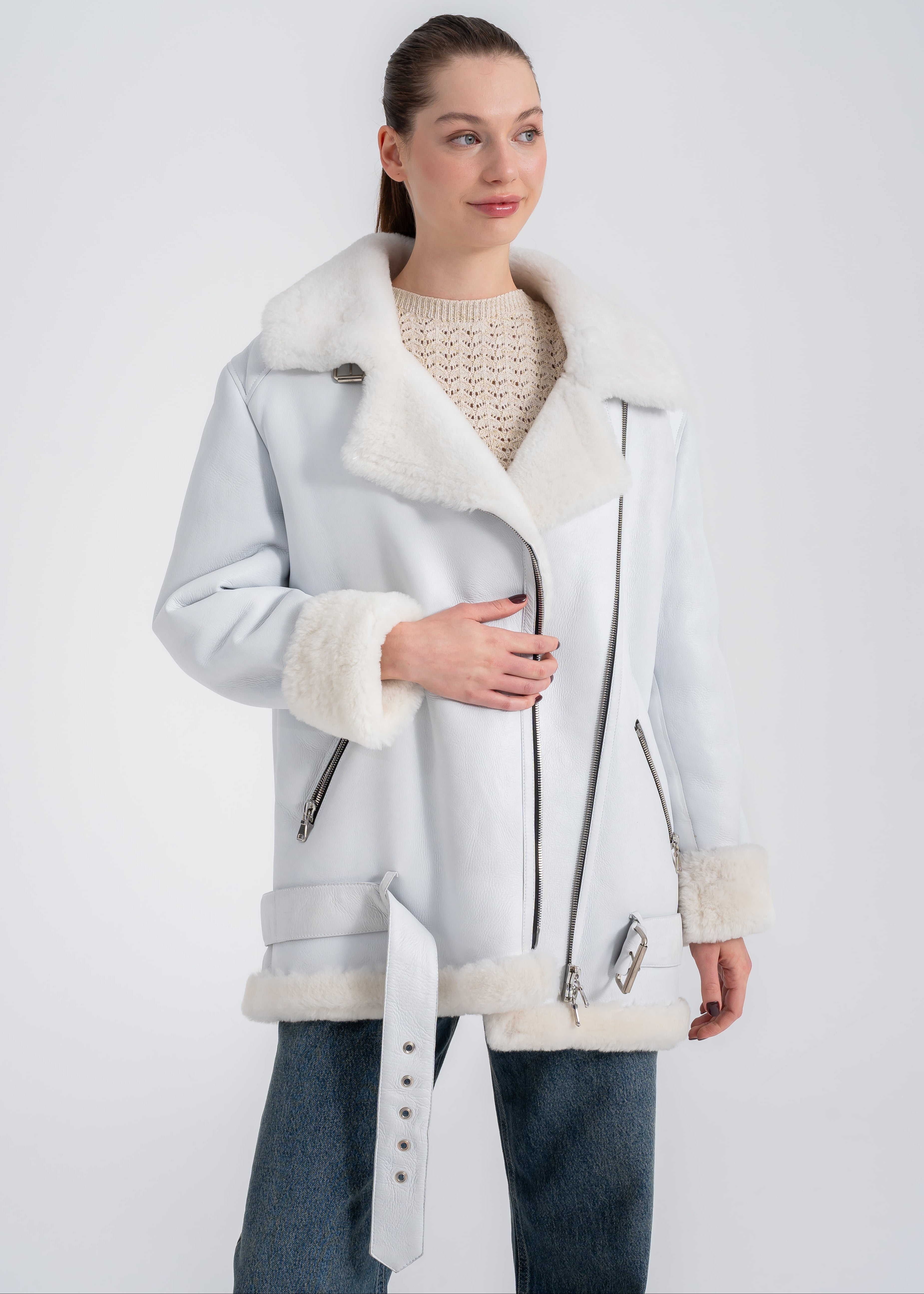 Woman wearing an oversized white shearling biker coat with wide lapels, asymmetric zipper and buckle hem detail by Lebeni.