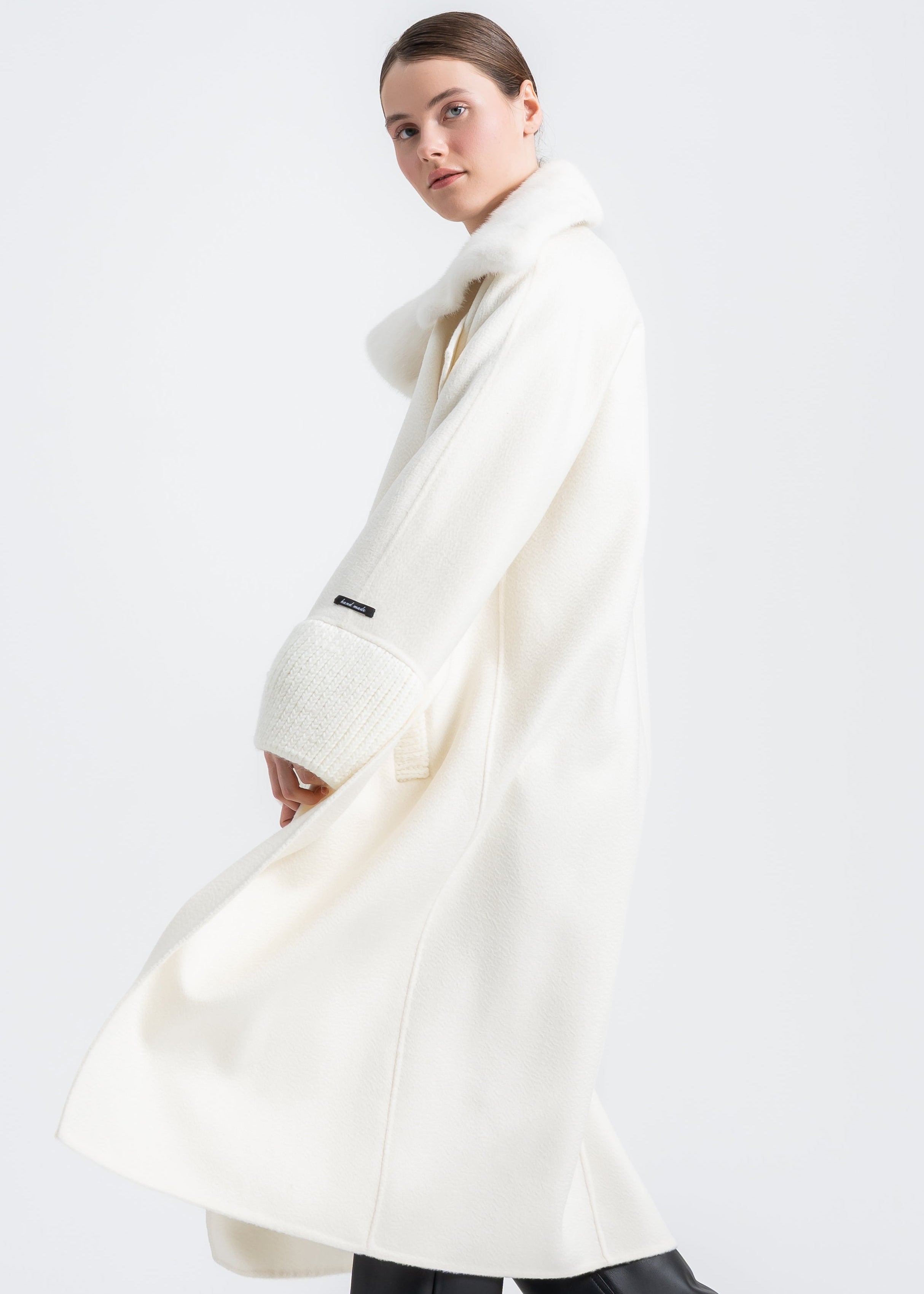Woman wearing a long winter white wool coat with real light beige mink fur shawl collar, wrap belted design, wide ribbed knit cuffs and knit trimmed front pockets by Lebeni.