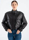 Woman wearing a black lambskin utility leather jacket with stand collar, large flap pockets, shoulder epaulettes, adjustable strap cuffs and satin lining styled with blue jeans by Lebeni.