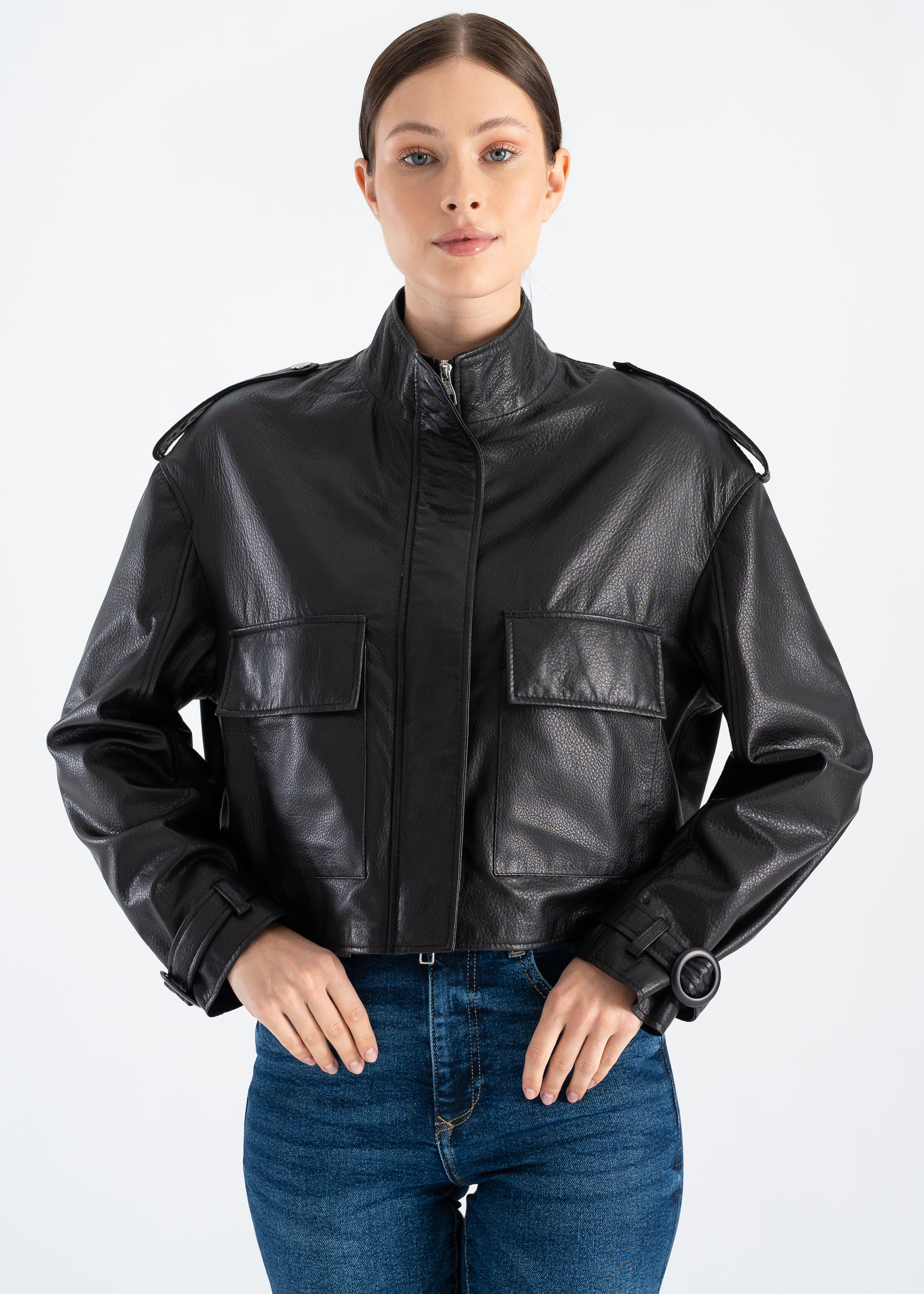 Woman wearing a black lambskin utility leather jacket with stand collar, large flap pockets, shoulder epaulettes, adjustable strap cuffs and satin lining styled with blue jeans by Lebeni.